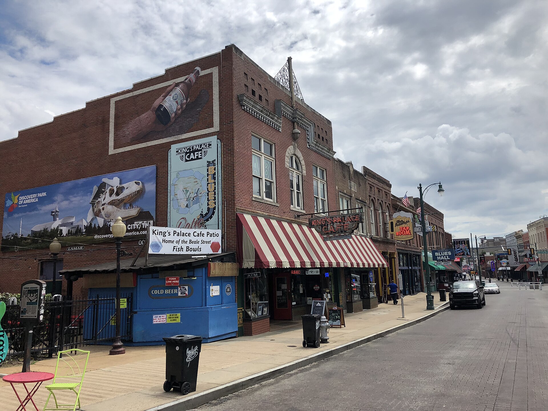 Quiet Beale Street with King's Palace Cafe's striped awning, painted brick murals and rows of blues club signs under cloudy skies