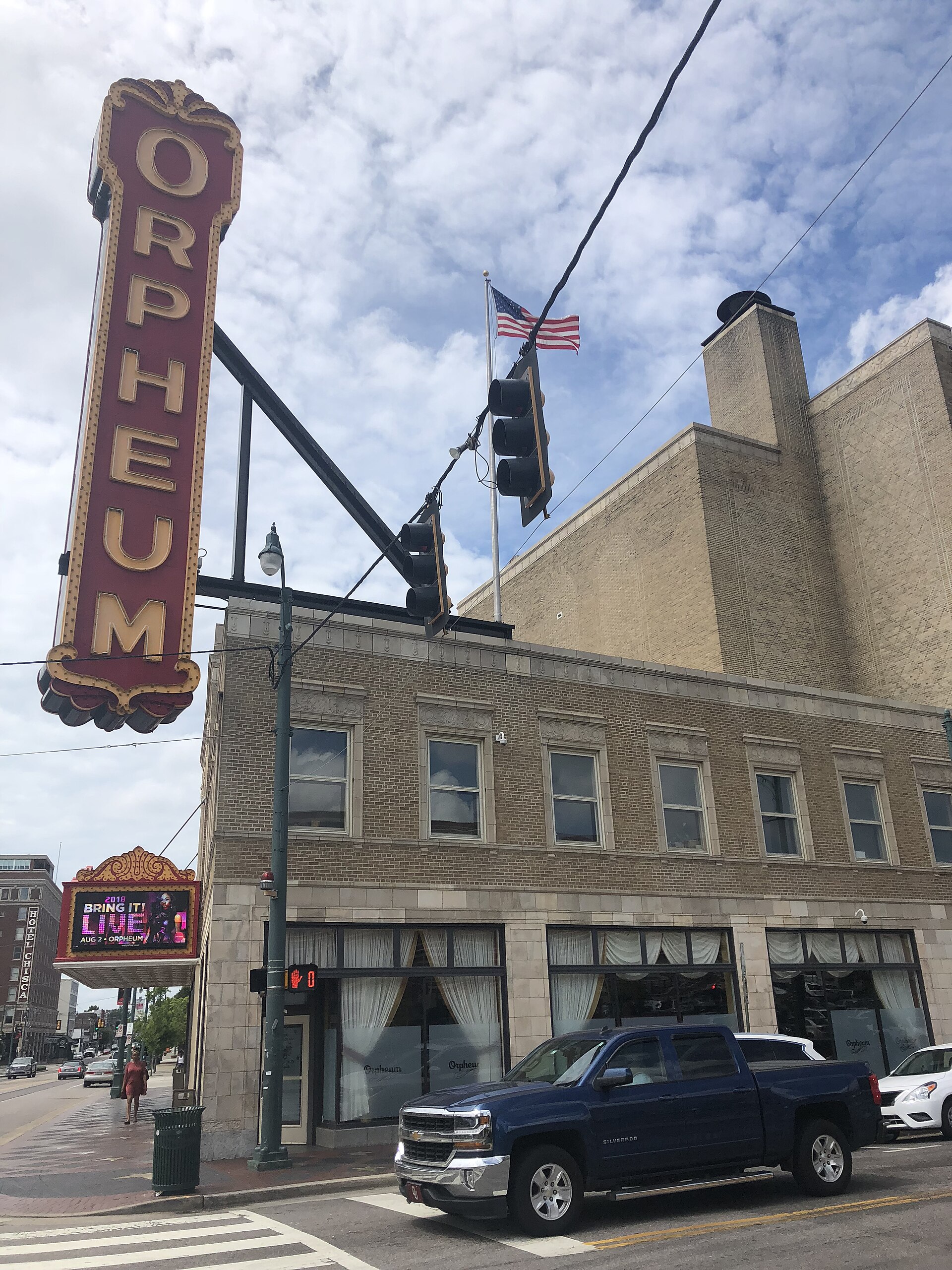 Tall vertical red Orpheum marquee sign on a brick theatre building, with a blue pickup truck parked at the corner