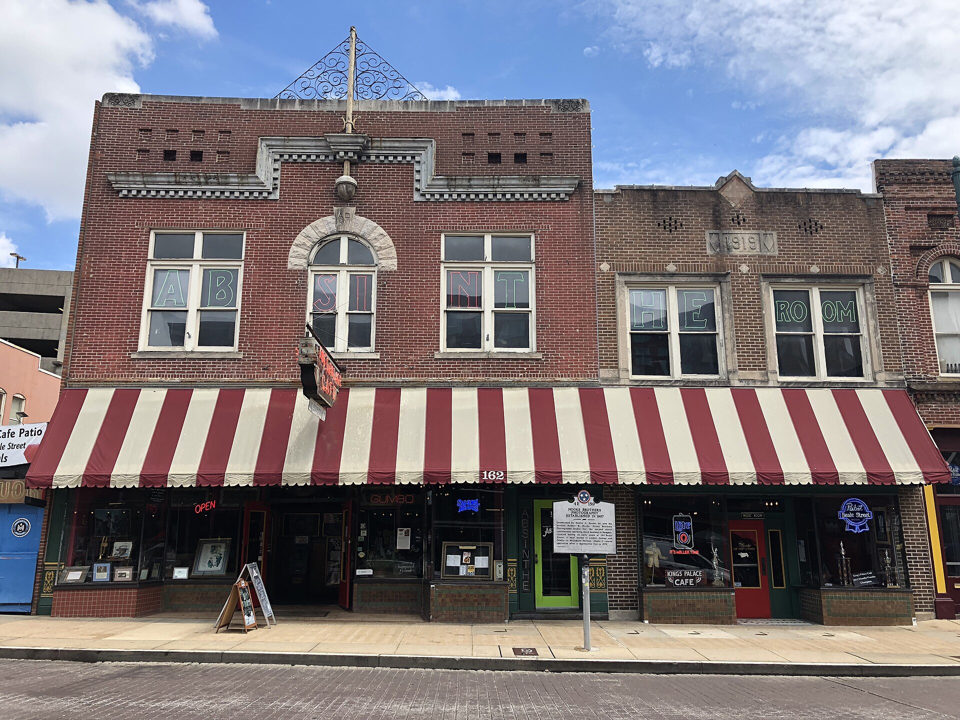 Red brick storefronts with a striped awning and "Absinthe Room" lettering across the upper windows on a quiet street