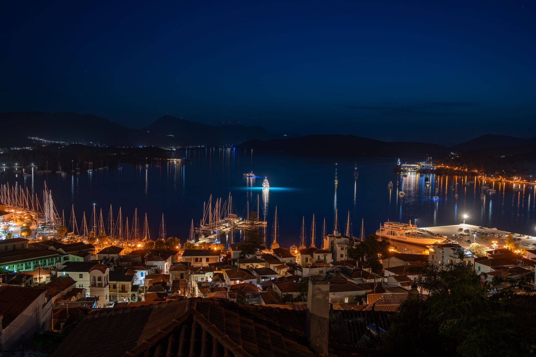 A vibrant aerial night view of a coastal town with illuminated streets and a serene harbor