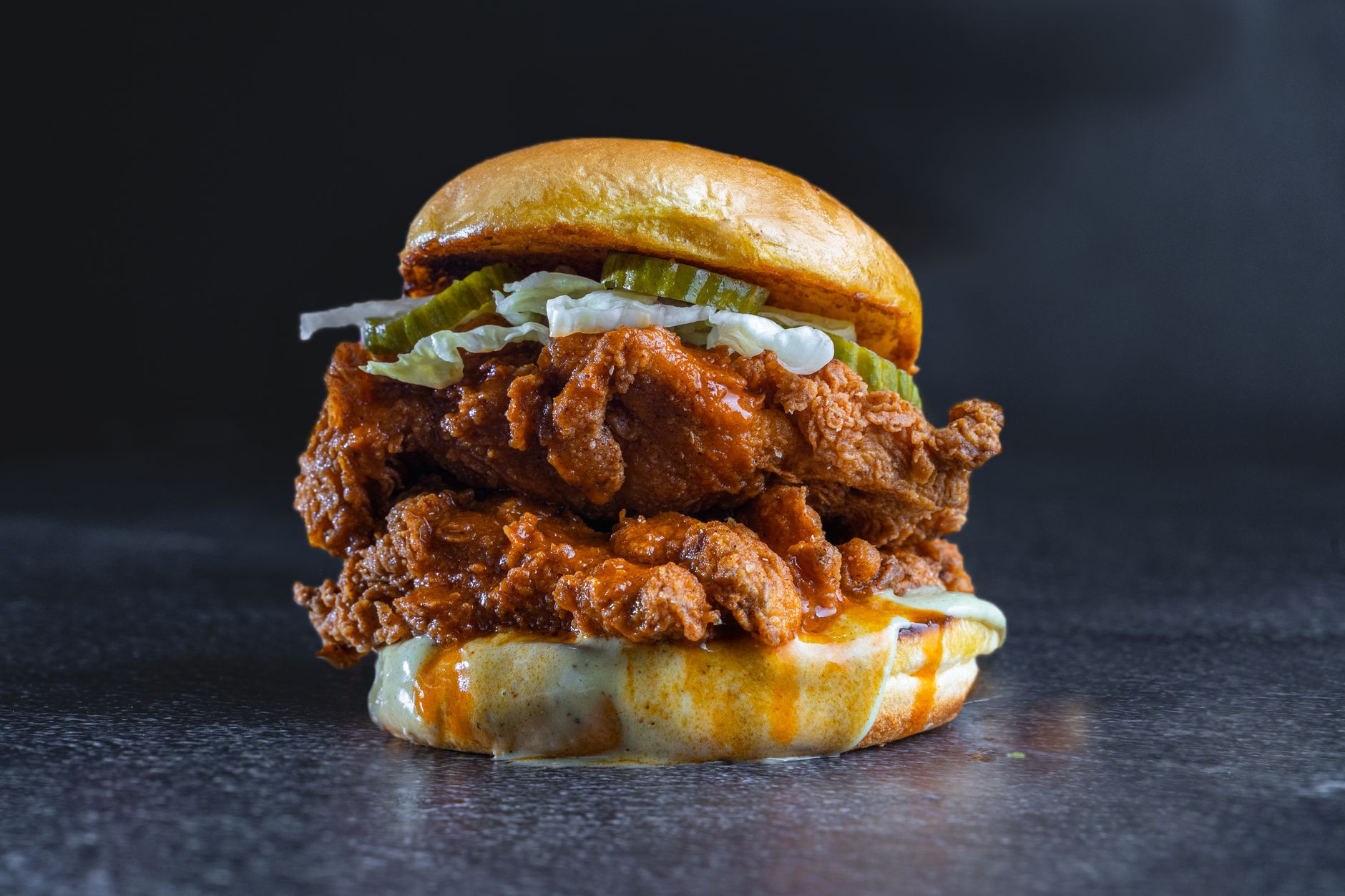 Fried chicken burger topped with pickles and creamy cheese sauce