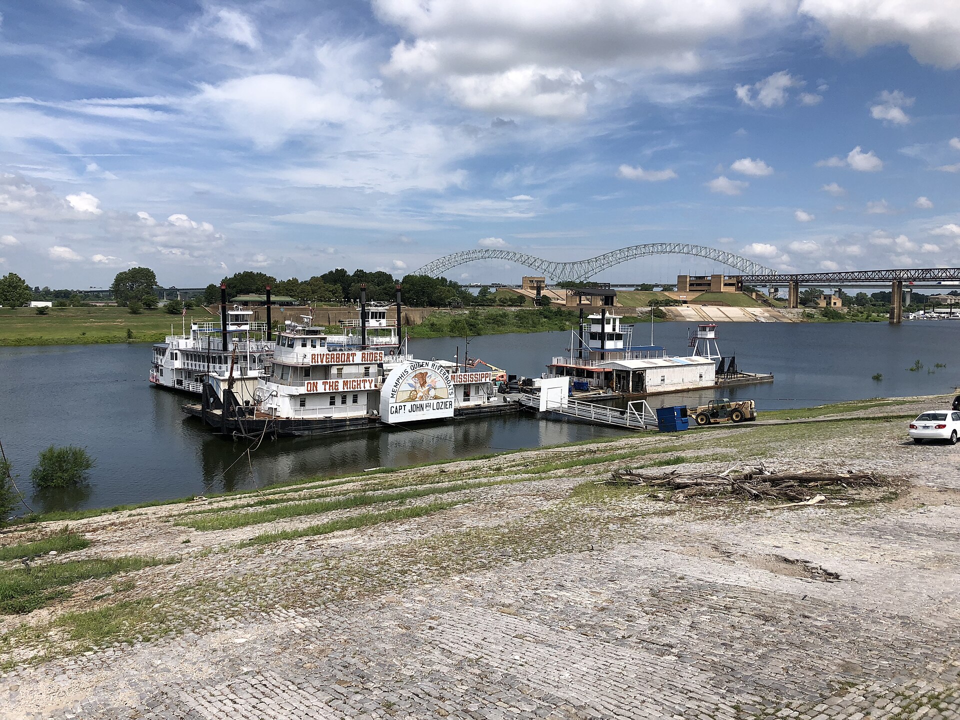 Riverboats offering rides moored along the Mississippi River in Memphis, with the arched Hernando de Soto Bridge behind