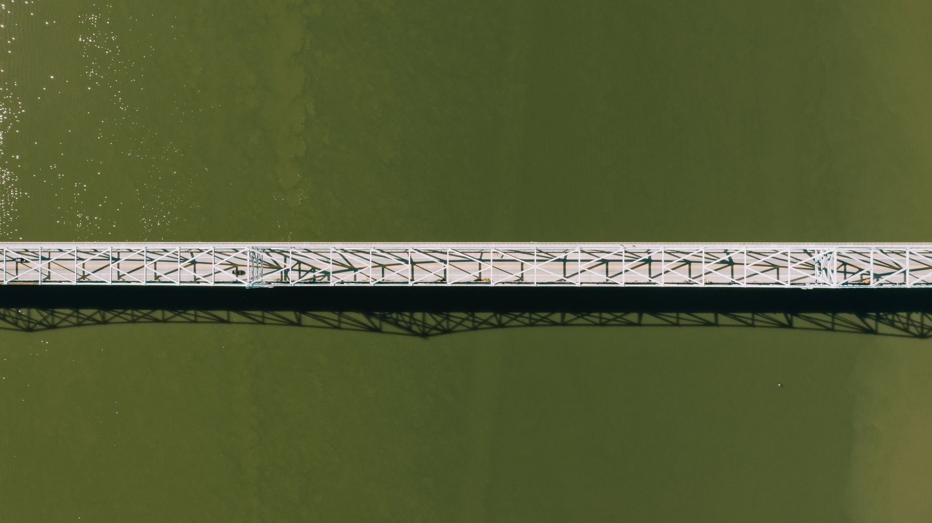 Aerial top view of a modern motor bridge crossing a vast rippling river on a sunny day